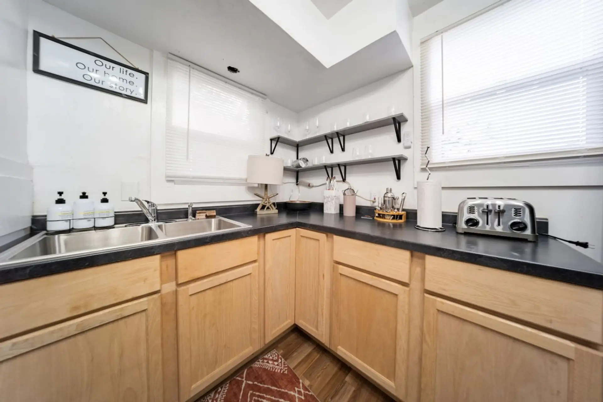 The kitchen is a bright and fully equipped space that blends classic wood cabinetry with modern black appliances and hardware. It features a double stainless steel sink, a gas range, a full-sized refrigerator, and essential countertop appliances like a to