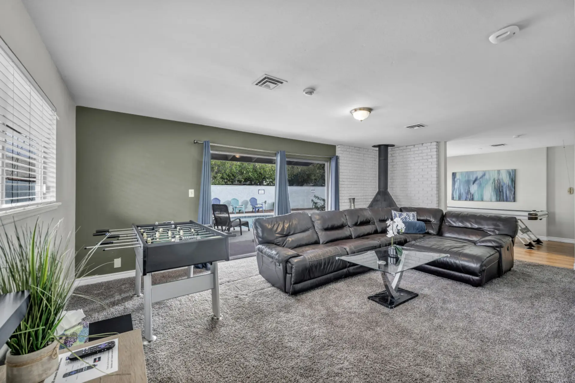 Spacious living area featuring a cozy leather sectional, foosball table, and a view of the pool. Perfect for unwinding, game nights, or enjoying indoor-outdoor living!