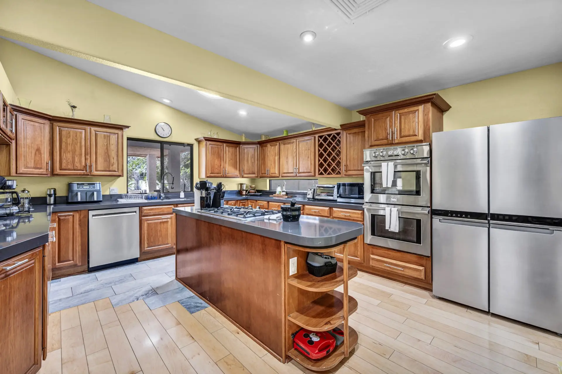 Feed the whole crowd with ease in this stunning, open chef's kitchen! Featuring an expansive center island with a gas cooktop, double ovens, an extra-large refrigerator, and beautiful wood cabinetry, it is fully stocked with all the modern appliances and 