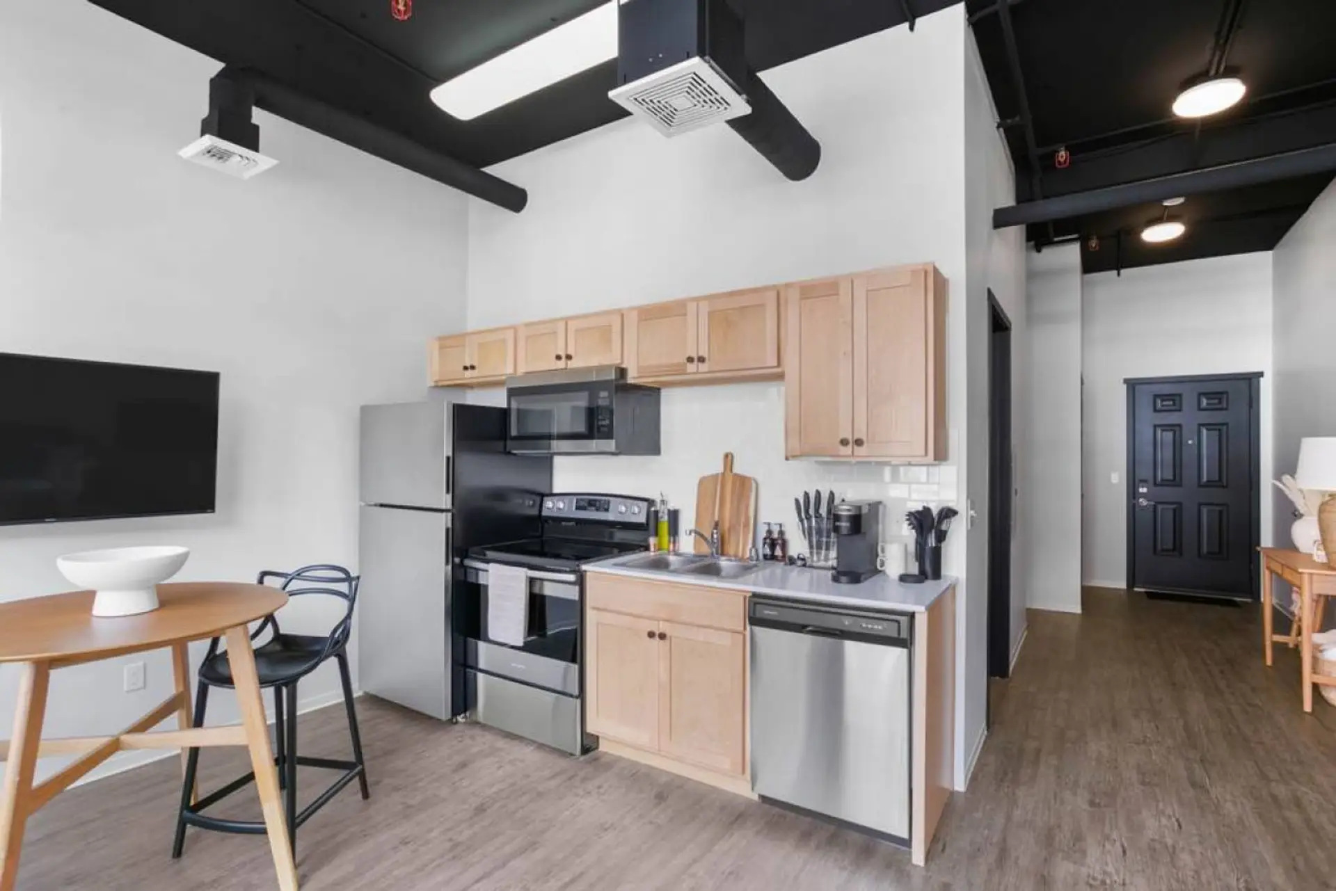 A galley kitchen with light wood cabinets, stainless steel appliances and a black bar stool.
