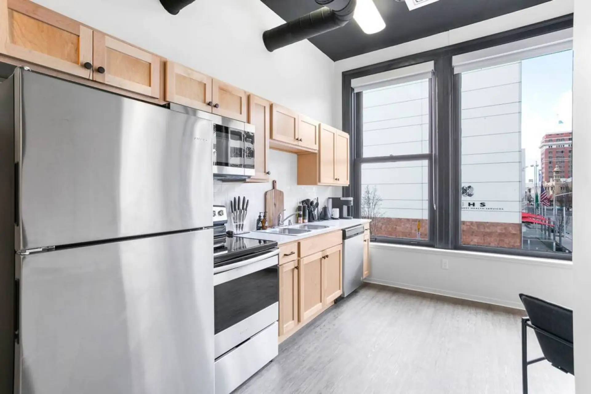 Light wood cabinets line the kitchen with white counters, a stainless steel refrigerator, range, and a window above the sink.