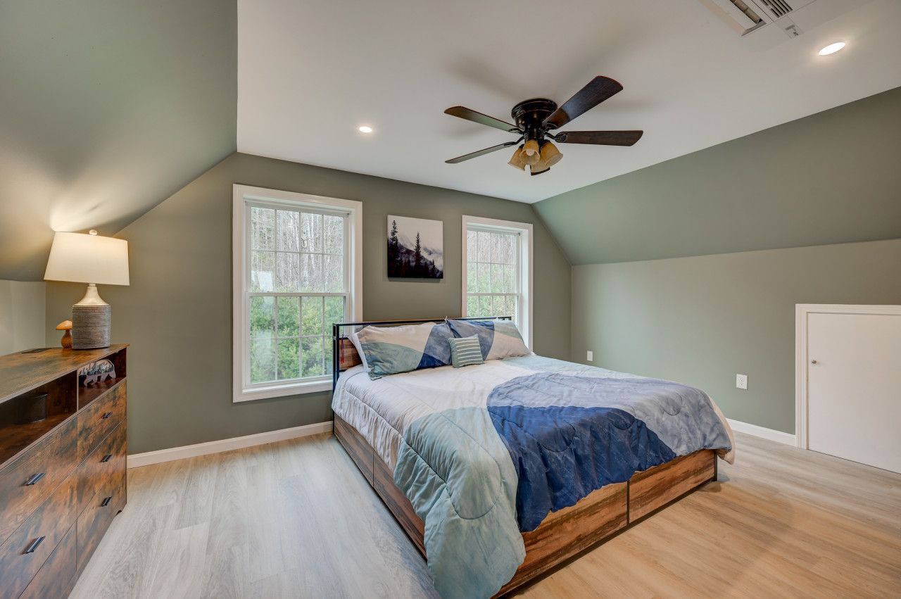 Spacious bedroom with a king bed, cozy decor, and panoramic forest views through large windows.