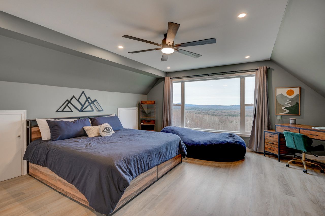 Spacious bedroom with a king bed, cozy decor, and panoramic forest views through large windows.