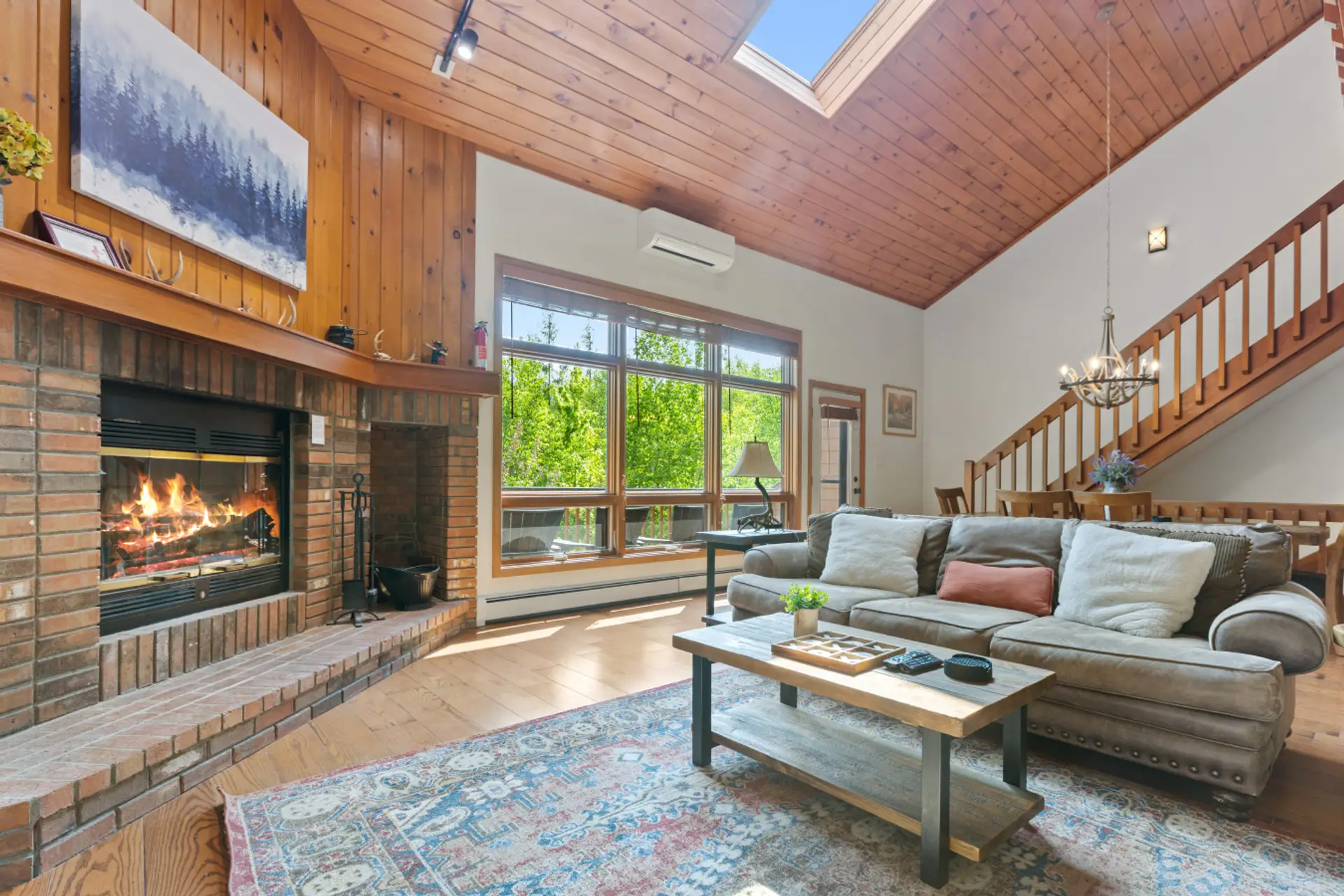 Open-concept living with forest views, deck access, cozy fireplace, and plush couches—perfect for relaxing or gathering together.