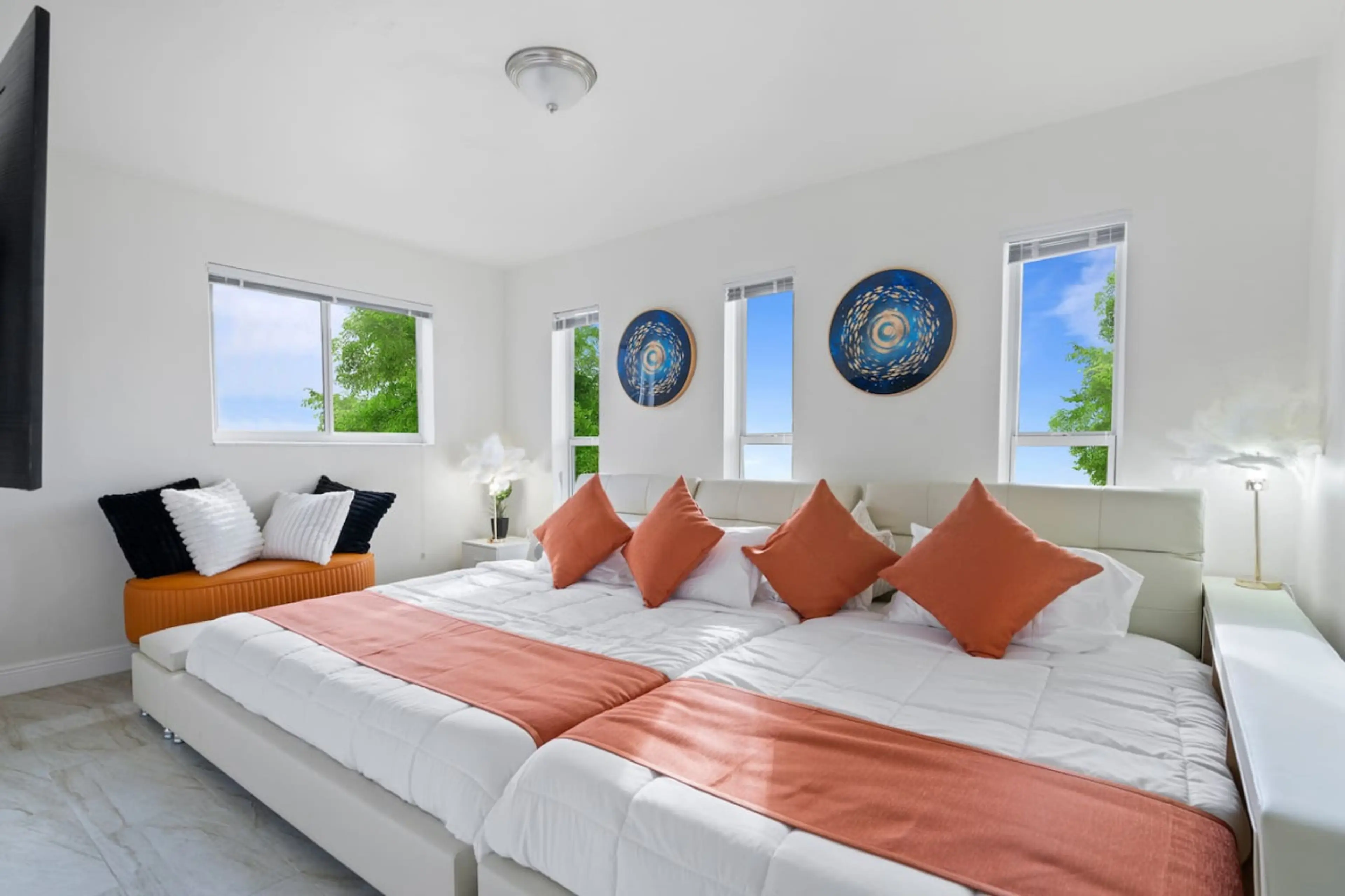 Serene master bedroom featuring two queen beds, abundant natural light through multiple windows, elegant coral accents & decorative wall art