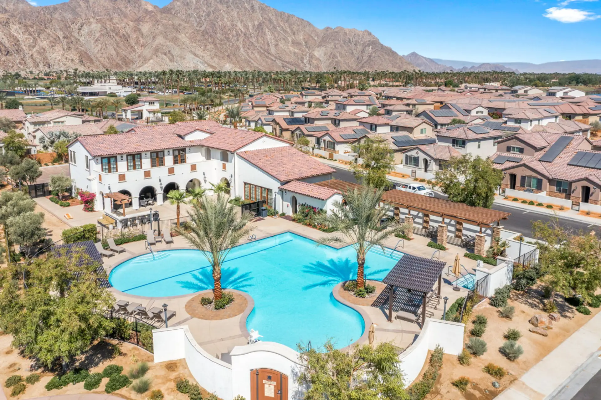 Resort-style pool & clubhouse surrounded by palm trees, w/ mountain views in the distance