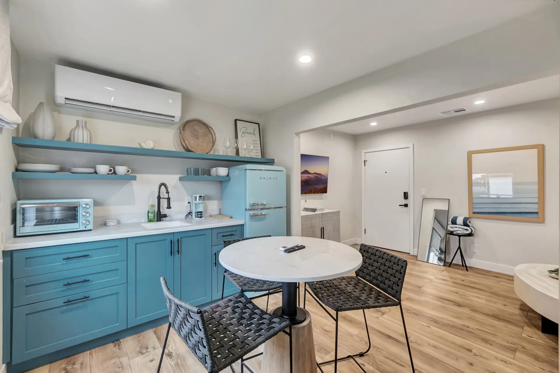 Bright studio w/ blue kitchenette, round dining table & cozy bed area in an open, airy layout