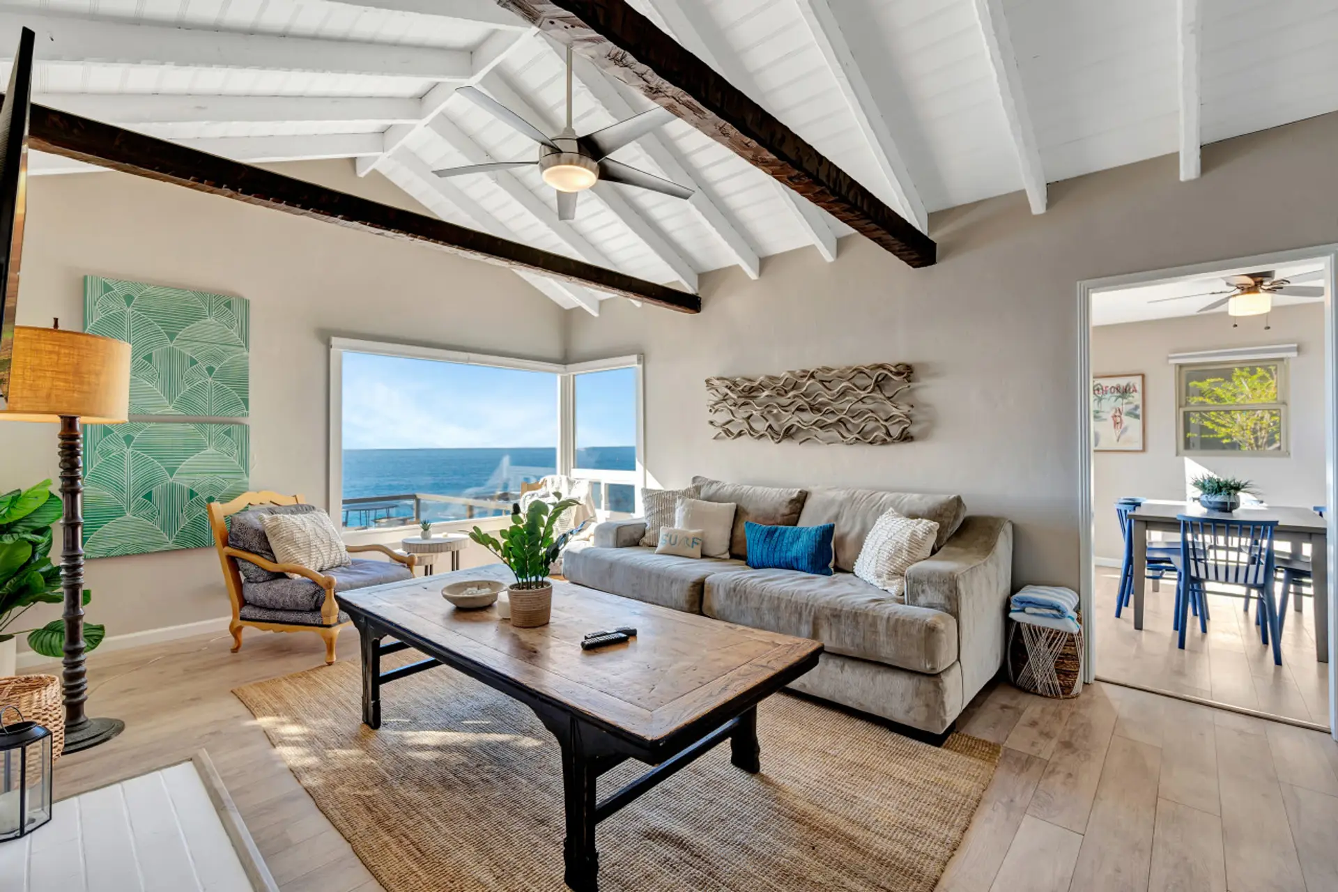 Bright living room w/ vaulted ceilings, exposed beams & picture window framing the ocean