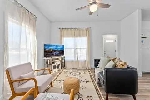 Living room with a leather sofa, two armchairs, a woven pouf, and a TV