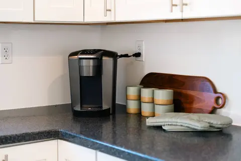 Single-serve coffee maker, canisters, and a cutting board on the counter
