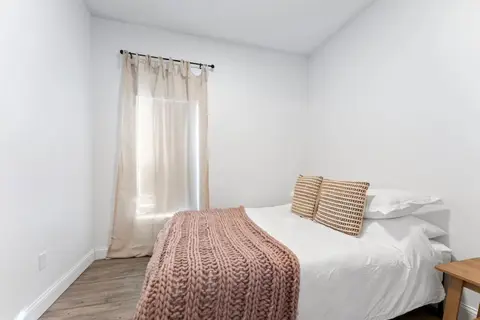 Bedroom with a queen bed and a pink knit throw under a curtained window