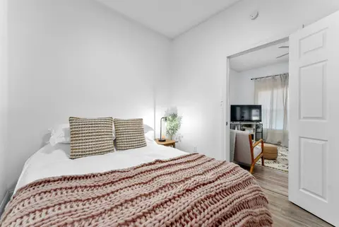 Bedroom with a queen bed and a knit throw, its door open to the living room