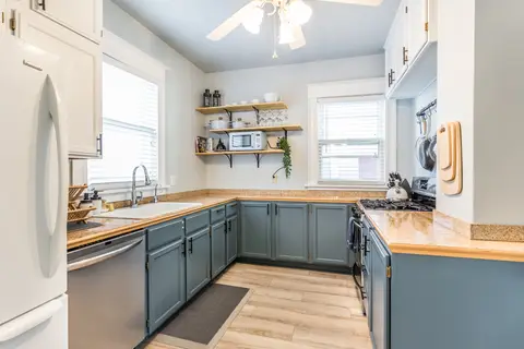 Kitchen with blue lower cabinets, butcher-block counters, and open shelves
