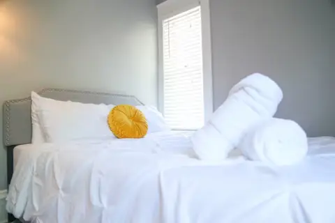 Queen bed with white bedding and a yellow accent pillow