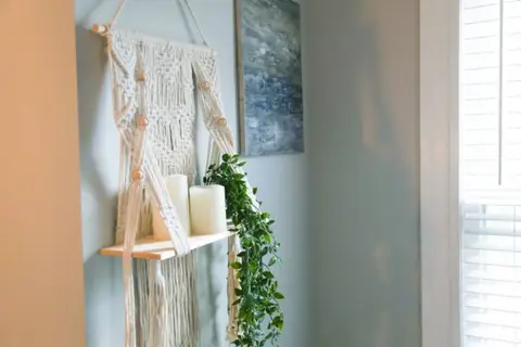 Macramé wall hanging and a small shelf with a candle and a plant
