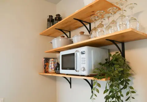 Open kitchen shelves with a microwave, wine glasses, and white serving dishes