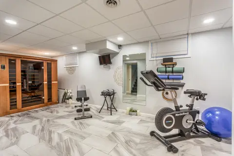 Lower-level gym with a spin bike, a weight bench, a mounted TV, and the sauna