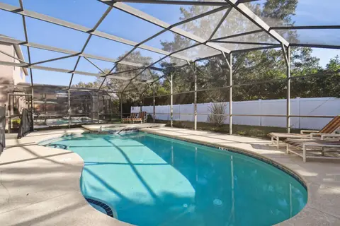 Screened pool deck with loungers along a white privacy fence