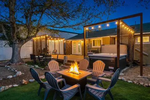 Gas fire table ringed by Adirondack chairs, with the hot tub and string lights behind