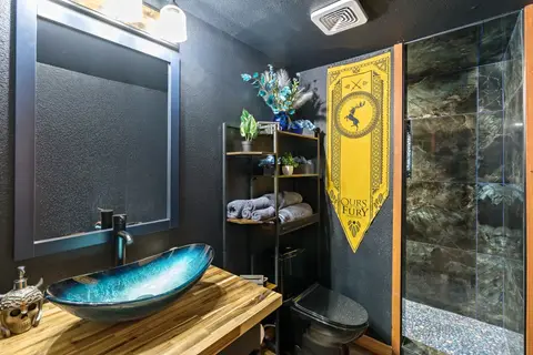 Blue glass vessel sink on a wood counter beside a dark tiled shower