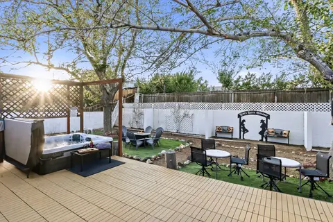 Backyard by day with the hot tub, a fire table, bistro tables, and shade trees