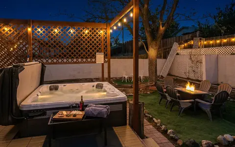 Hot tub beside a lattice screen with string lights, the fire table beyond