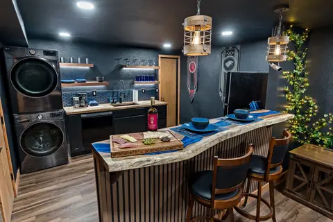 Blue epoxy river bar with two stools and lit ivy, beside a stacked washer and dryer
