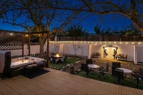 Backyard at dusk with the hot tub, a gas fire table, bistro tables, and the cowboy mural