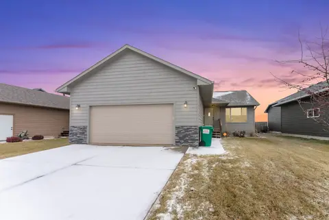Front of the gray house with a two-car garage and a wide driveway at dusk