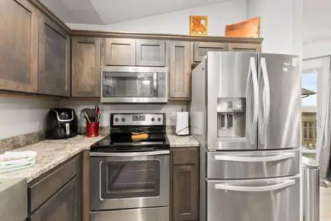 Stainless refrigerator, range, and microwave between dark wood cabinets