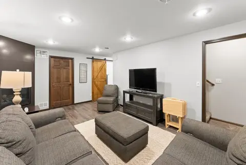 Den with a gray sofa, an ottoman, a TV, and a sliding barn door