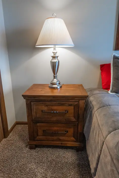 Wood nightstand with a silver table lamp beside the bed