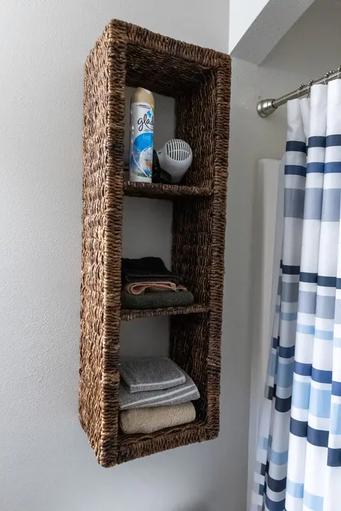 Woven wall shelf with towels beside the shower curtain
