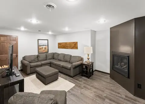 Den with a gray sectional, an ottoman, a TV, and a fireplace
