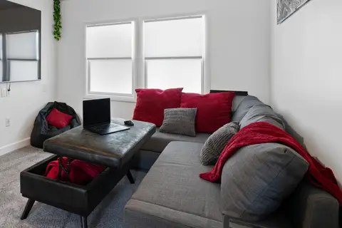 Gray sectional with red pillows and a storage ottoman on gray carpet