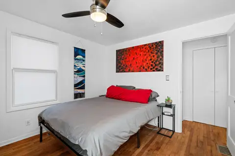 Queen bed with red pillows under a red painting, beside a side table