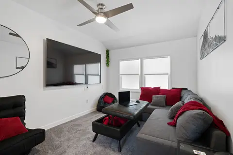 Den with a gray sectional, a storage ottoman, and a large wall-mounted TV