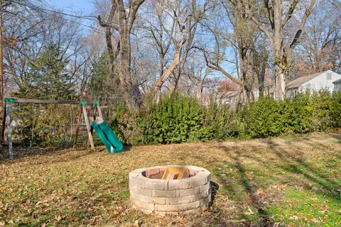 Stone fire pit on the lawn, with a swing set and slide behind