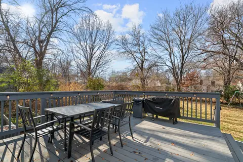 Deck with a dining table, chairs, and a covered grill, overlooking the backyard