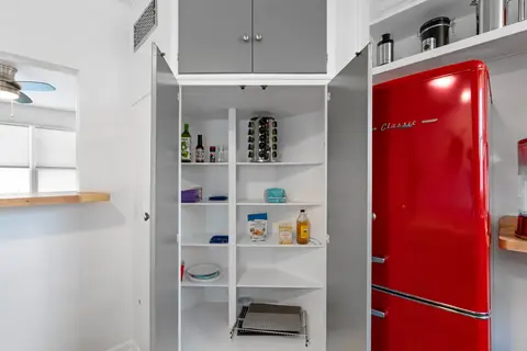 Pantry cabinet with shelves of dry goods next to the red fridge