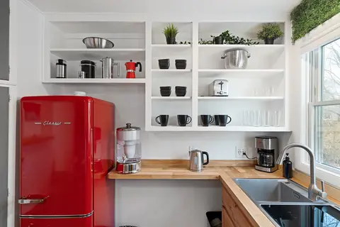 Red fridge beside open shelving, a coffee maker, and a sink under the window
