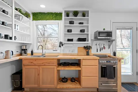 Kitchen with open shelves, a sink under the window, and a stainless range