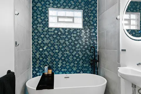 Freestanding soaking tub against a wall of teal fish-scale tile