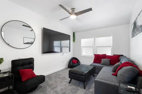 Carpeted den with a gray sectional, a lounge chair, and a large wall-mounted TV