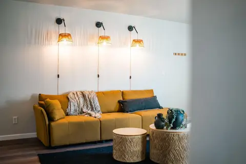 Mustard sofa under three lit wall sconces, with round woven side tables