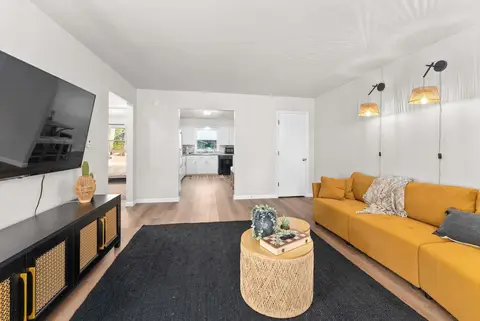 Long living room with a mustard sofa and wall sconces, looking toward the kitchen