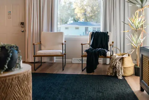 Two armchairs by the front window, with a navy rug and a potted palm