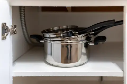 Stainless steel pots and a pan in a lower cabinet