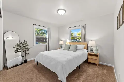 Bedroom with a queen bed, an arched floor mirror, a potted tree, and two windows