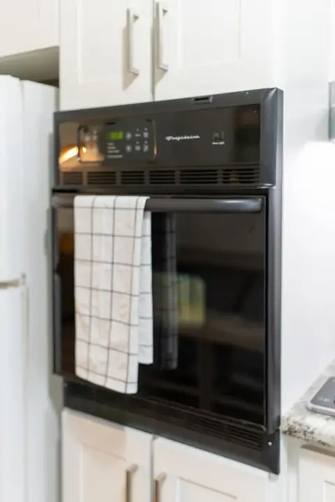 Black wall oven with a checked dish towel on the handle